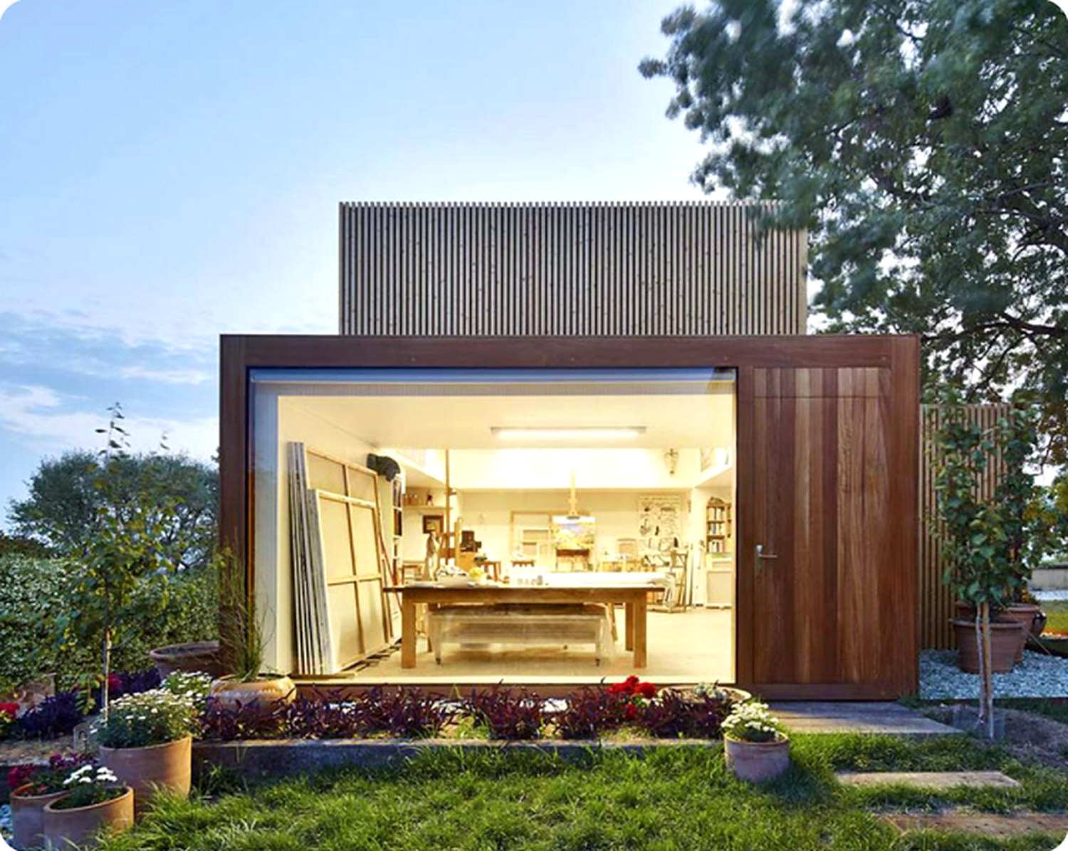 Artist's garden studio with a wide glazed opening, a worktable and canvases inside